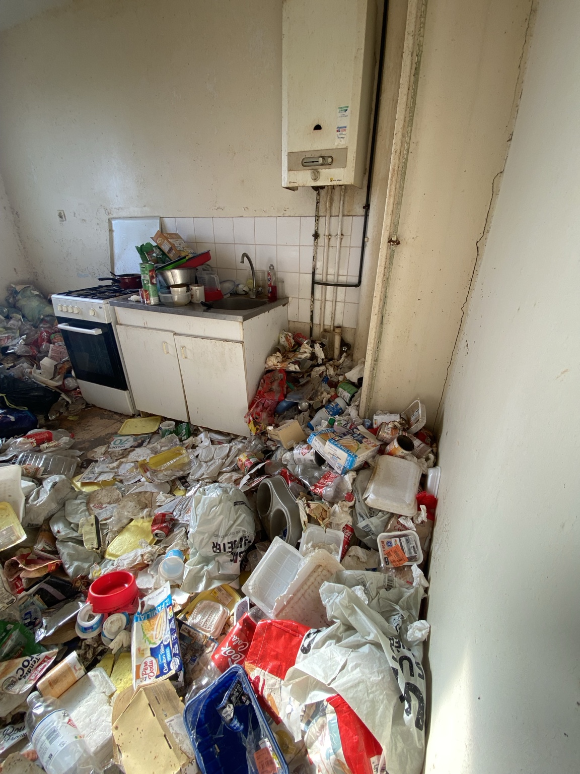 Cuisine dont le sol et l’accès aux équipements sont encombrés d’emballages et de déchets.